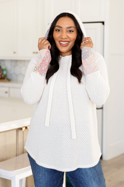 Made with soft and lightweight waffle knit, this hoodie features playful floral accents, a cozy hood, and a unique scooped hem