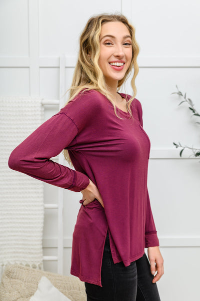 The Long Sleeve Knit Top With Pocket In Burgundy features a lightweight, stretchy fabric that shapes a round neckline with long sleeves, and a hi-low hem with side slits.