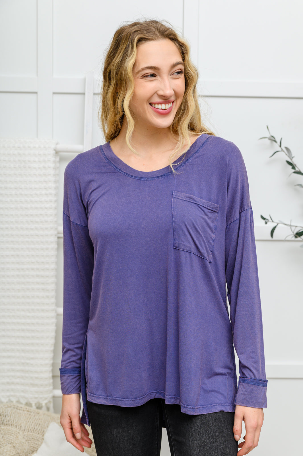 The Long Sleeve Knit Top With Pocket In Denim Blue features a lightweight, stretchy fabric that shapes a round neckline with long sleeves, and a hi-low hem with side slit