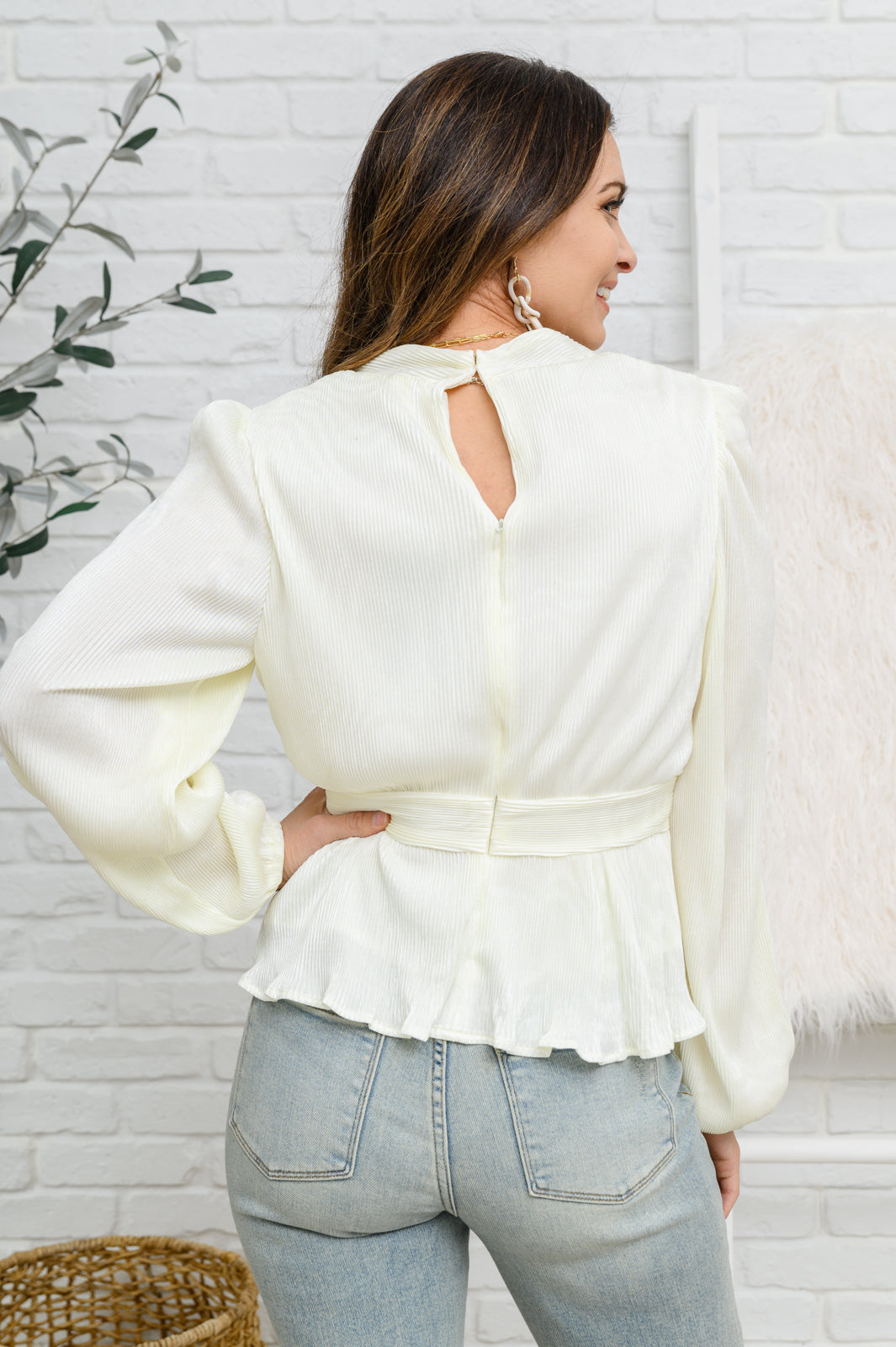 A stunning plisse fabric shapes a v neckline that drops into a peplum style waist, with long balloon sleeves, finished with a puff shoulder detail and elastic cuffs.